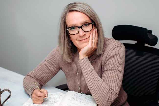 Participant Kelli - person in brown sweater sitting at a table with a journal