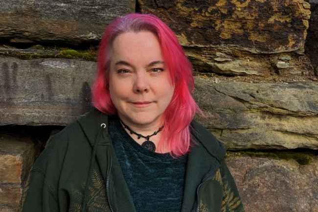 Participant Lee - person with pink hair smiling in front of a large rock
