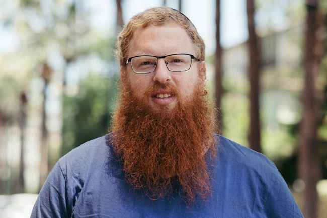 Deconstructing Stigma participant Yoel - portrait of person with red hair and long beard, glasses, blue shirt
