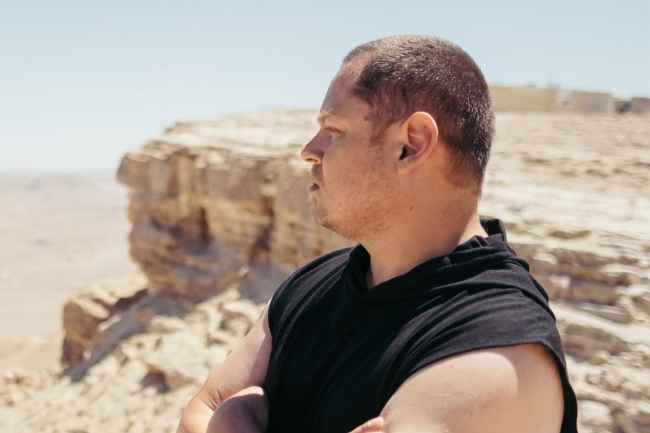 Deconstructing Stigma participant Lavih - Person stands outside in desert with boulder behind