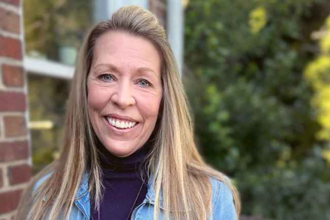 Participant Renee - person with long blond hair in a jean jacked smiling in front of greenery