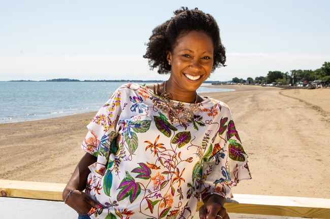 Participant Ivy - person with short curly hair smiling in front of a beach