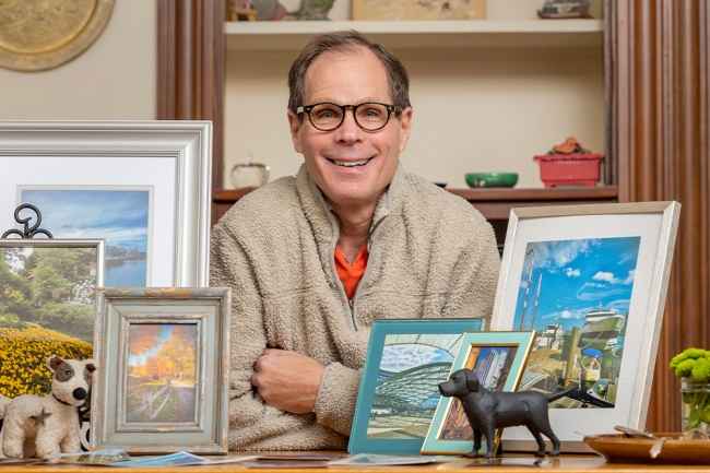 Participant David - person with short dark hair and glasses smiling in front of shelves with artwork