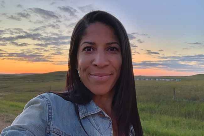 Participant Bianca - person with long dark hair smiling in front of a blue and orange sky