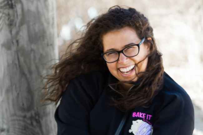 Participant Dayna - person with long and dark wavy hair and glasses smiling