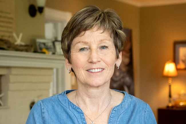 Participant Ann - person with short blond hair smiling in a room with a lamp