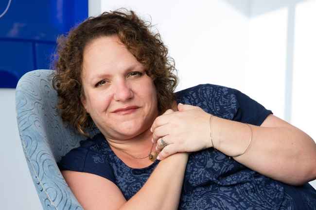 Participant Jamie - person with curly auburn hair smiling in a blue chair