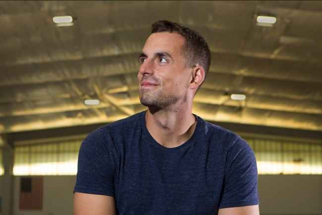 Person with short dark hair looking to the side, in the background is a large space with a high ceiling