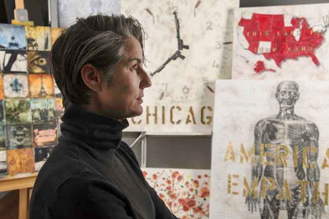 Participant Kelly wearing a black turtle neck and there is artwork in the background