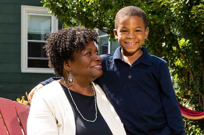 Participant Cynthia - person with dark curly hair sitting in a red chair and smiling with a young child