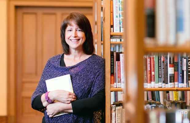 Participant Lise - person with dark hair wearing a purple sweater smiling near shelves of books