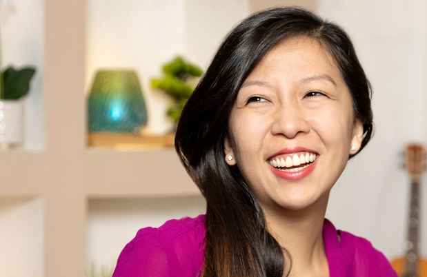 Participant Lena - person with long dark hair in a pink blouse smiling in front of a bookshelf