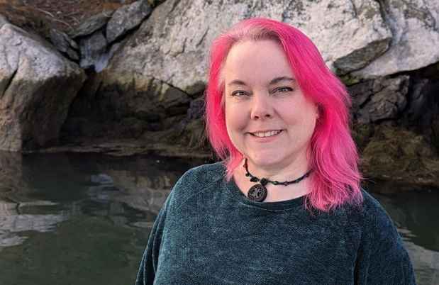 Participant Lee - person with pink hair smiling in front of a large rock