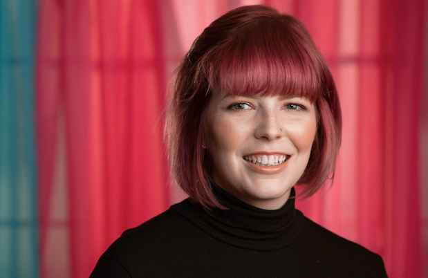 Participant Katherine - person with short, red, hair standing in front of colorful curtains