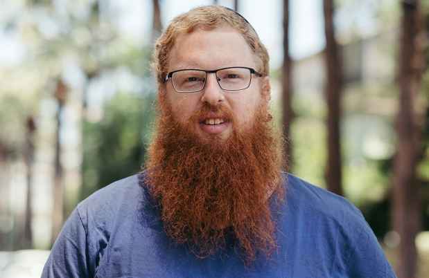 Deconstructing Stigma participant Yoel - portrait of person with red hair and long beard, glasses, blue shirt