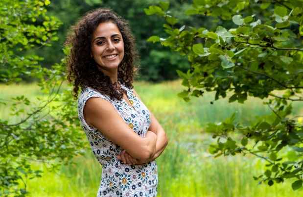 Participant Ream - person with dark curly hair in a floral dress smiling among trees