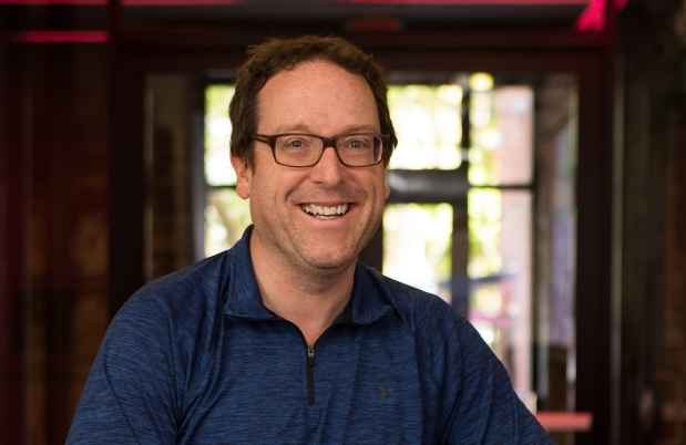 Participant Thomas - person with short brown hair and glasses smiling in a hallway with red lighting