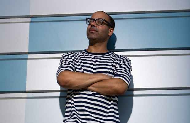 Participant Richard - person with short hair and glasses in a striped shirt leaning against a blue geometric wall