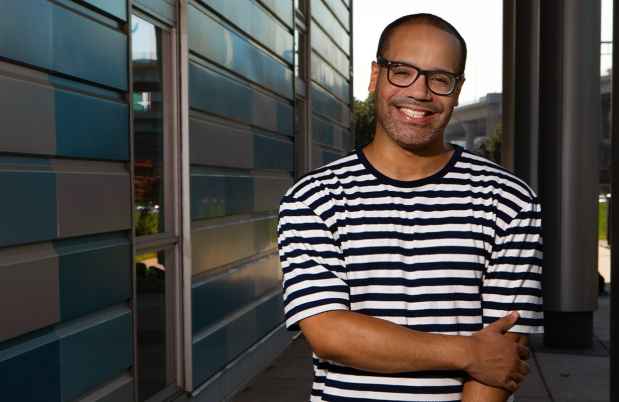 Participant Richard - person with short hair and glasses in a striped shirt smiling in front of a blue geometric wall