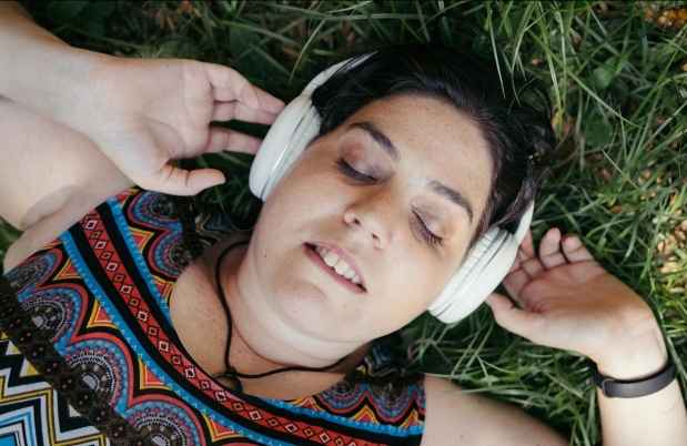 Deconstructing participant Noam - person in patterned tank top lies in grass, eyes closed, headphones on
