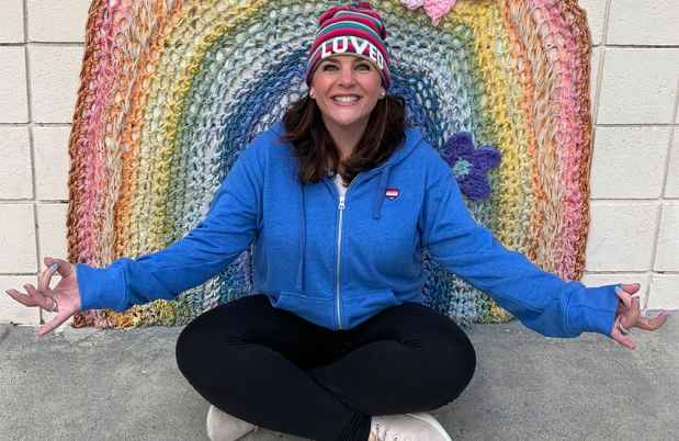 Participant Adrian sitting cross-legged in front of a crocheted rainbow