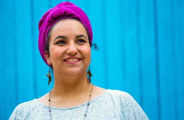 Deconstructing Stigma participant Leah Roni - person in headscarf against bright blue fence