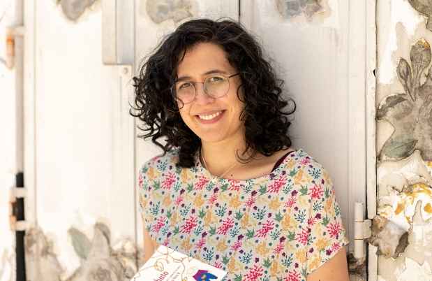 Deconstructing Stigma participant Jimena - Person in flowery shirt leans agains metal wall reading a book
