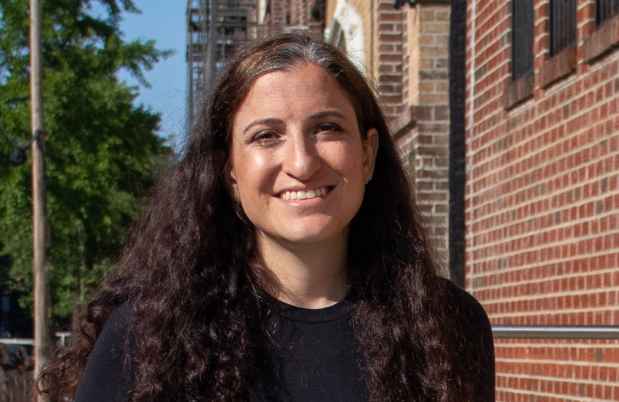 Participant Michelle - person with long, dark, wavy hair outside in front of a brick building