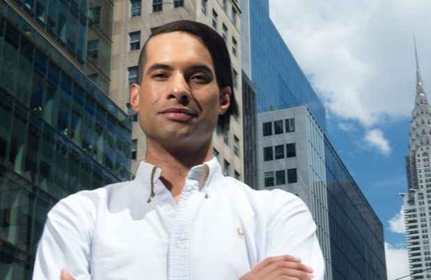 Participant Paul - person with short dark hair wearing a white shirt in front of a city skyline