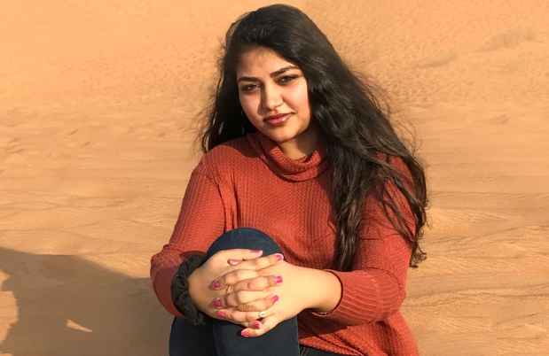 Participant Ramya - person with long dark hair in a red sweater sitting in sand