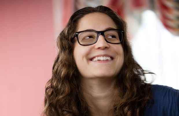 Participant Meredith - person with wavy brown hair and glasses smiling in front of a window