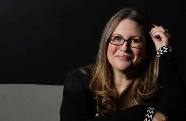 Participant Miriam - person with brown hair and glasses in front of a dark background