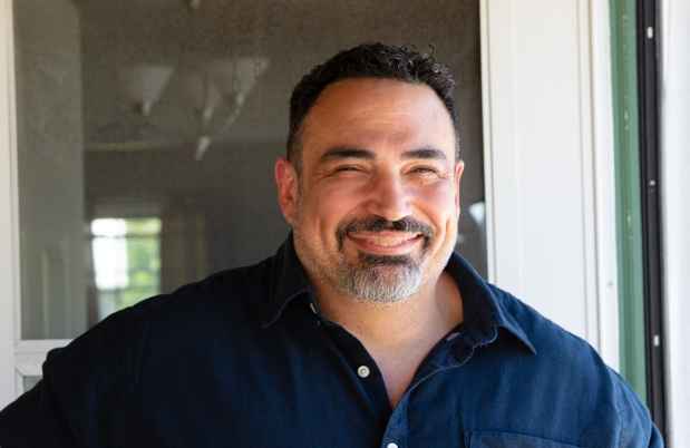 Participant Wayne - person with short dark hair smiling outside a door