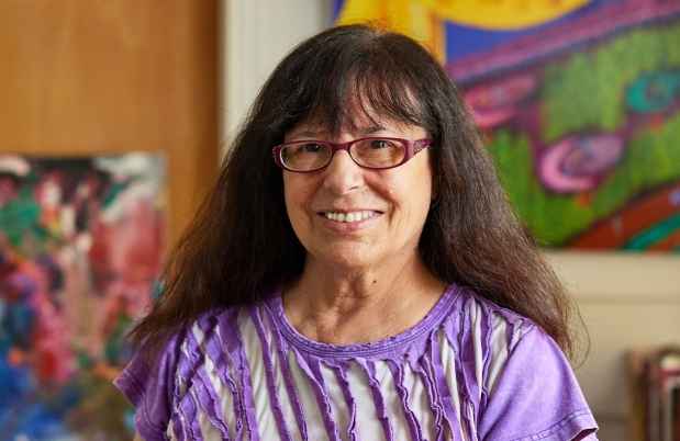 Participant Irene - person with long dark hair and glasses smiling in a colorful room