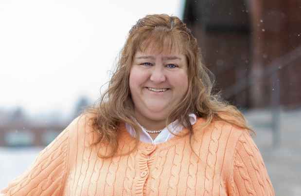 Participant Jodi - person with long auburn hair smiling outside on stairs while snow falls