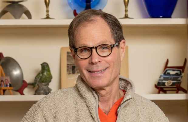 Participant David - person with short dark hair and glasses smiling in front of shelves with artwork