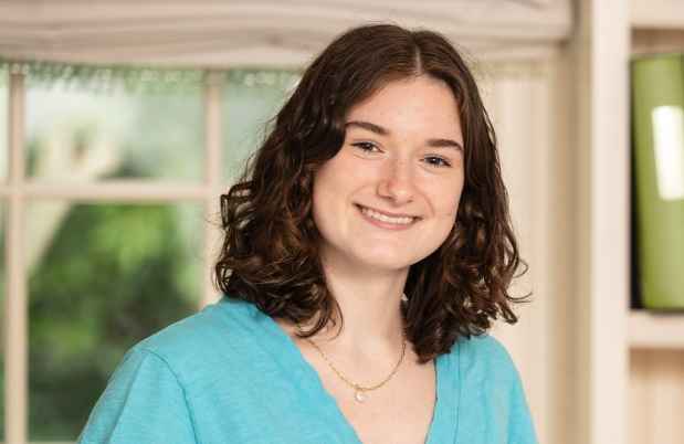 Participant Caroline - person with short brown hair smiling in front of a window and a bookshelf