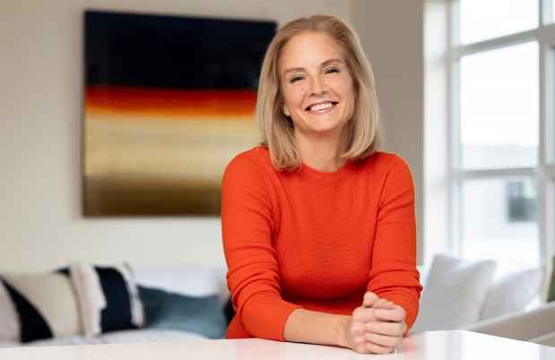 Participant Carrie - person with shoulder-length blond hair wearing an orange shirt and smiling