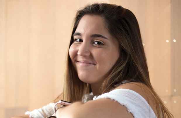 Participant Ana - person with long brown hair smiling and leaning on a red chair