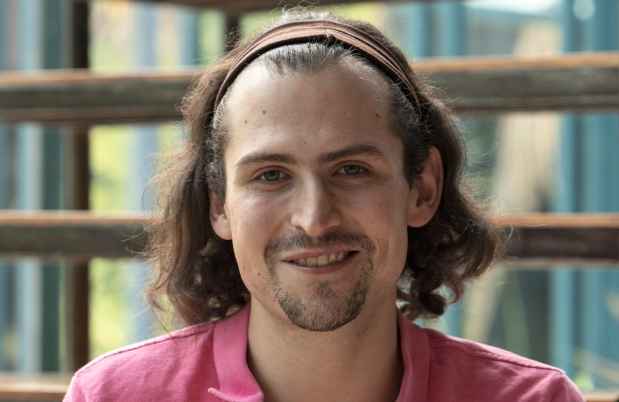 Participant Joaquín - person with shoulder-length brown hair smiling in front of a large window