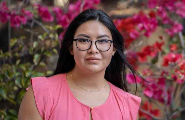 Participant Kaylee - person with long dark hair and glasses outside surrounded by pink flowers