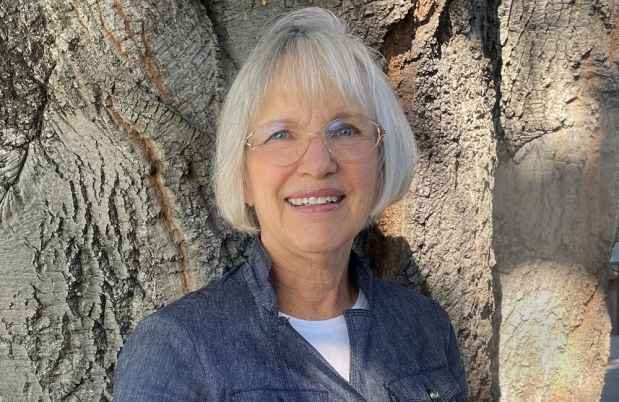 Participant Barbara - person with short white hair smiling in front of a tree trunk