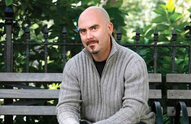 Participant Bruce - person with dark facial hair sits on a bench surrounded by greenery