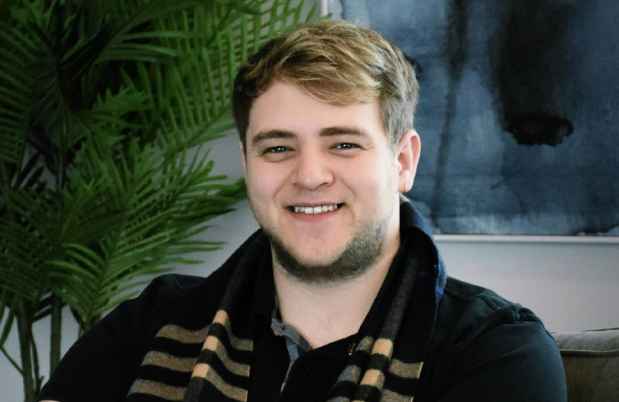 Participant Jay - person with short brown hair sitting in front of a houseplant and a painting