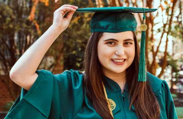Participant Carly - person with long auburn hair smiling and wearing a green graduation cap and gown