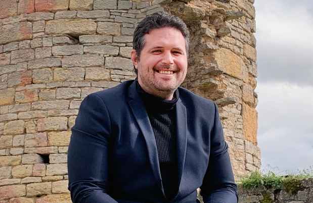 Participant Christophe - person with short dark hair smiling outside in front of a stone structure