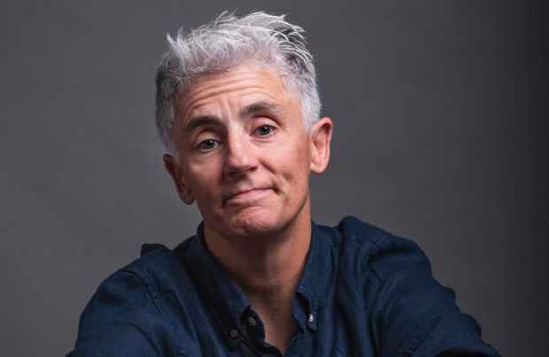Participant Christy - person with short white hair posing in front of a dark grey background