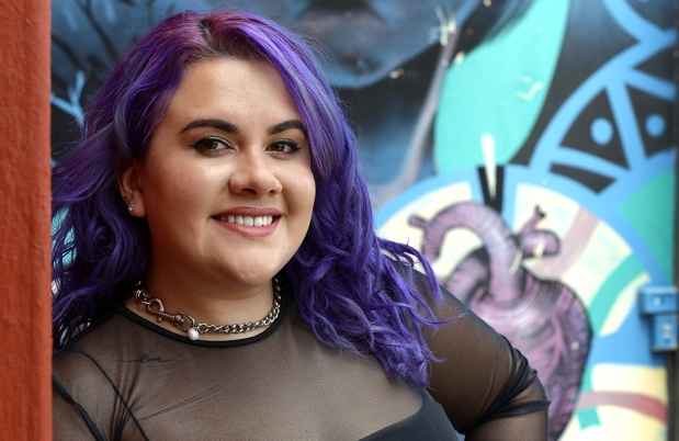 Participant Joanne - person with purple hair smiling in front of a colorfully painted wall
