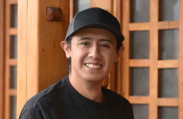 Participant Jimmy - person with short dark hair wearing a black baseball hat and smiling outside a wooden building