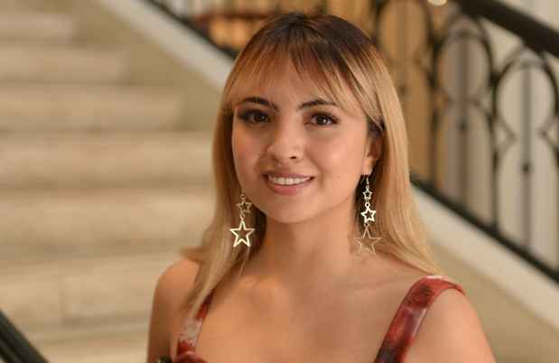 Participant Valeria - person with brown hair wearing star-shaped earrings and a red tank top smiling near a set of stone stairs